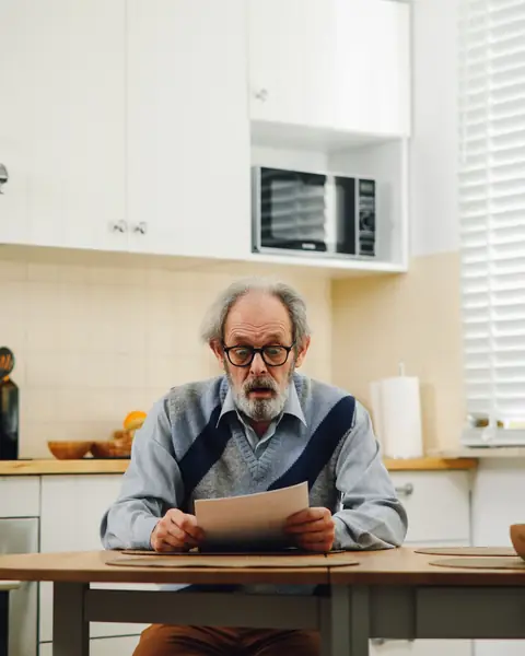 Hombre mayor con gafas leyendo un documento en la mesa de la cocina